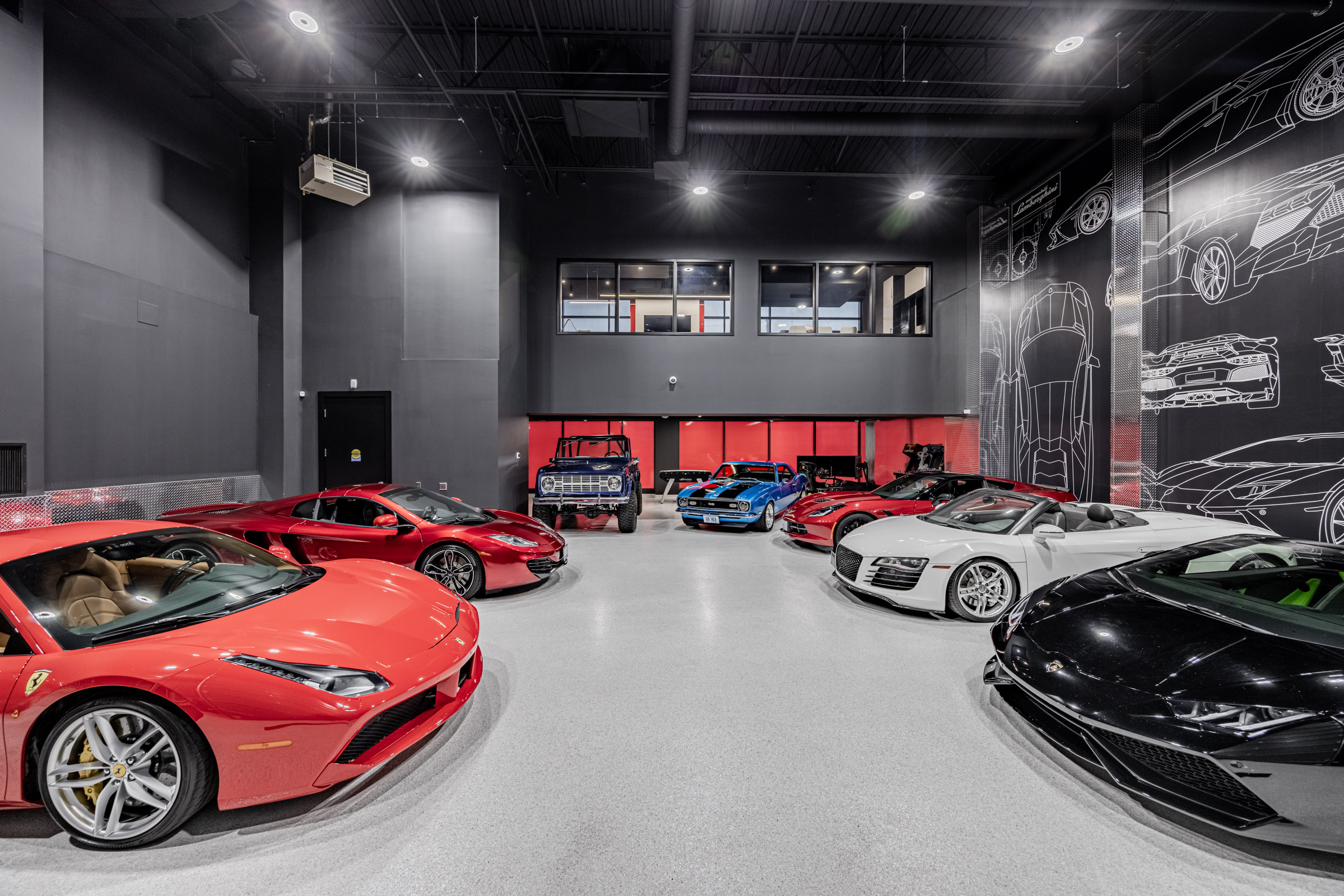 A private collection of exotic and classic cars inside a two-storey industrial showroom in Burlington, Ontario, with a blueprint-style mural on the far wall.
