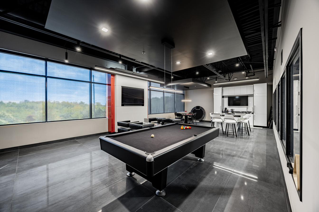 Second-floor lounge with pool table and kitchen, daylight.